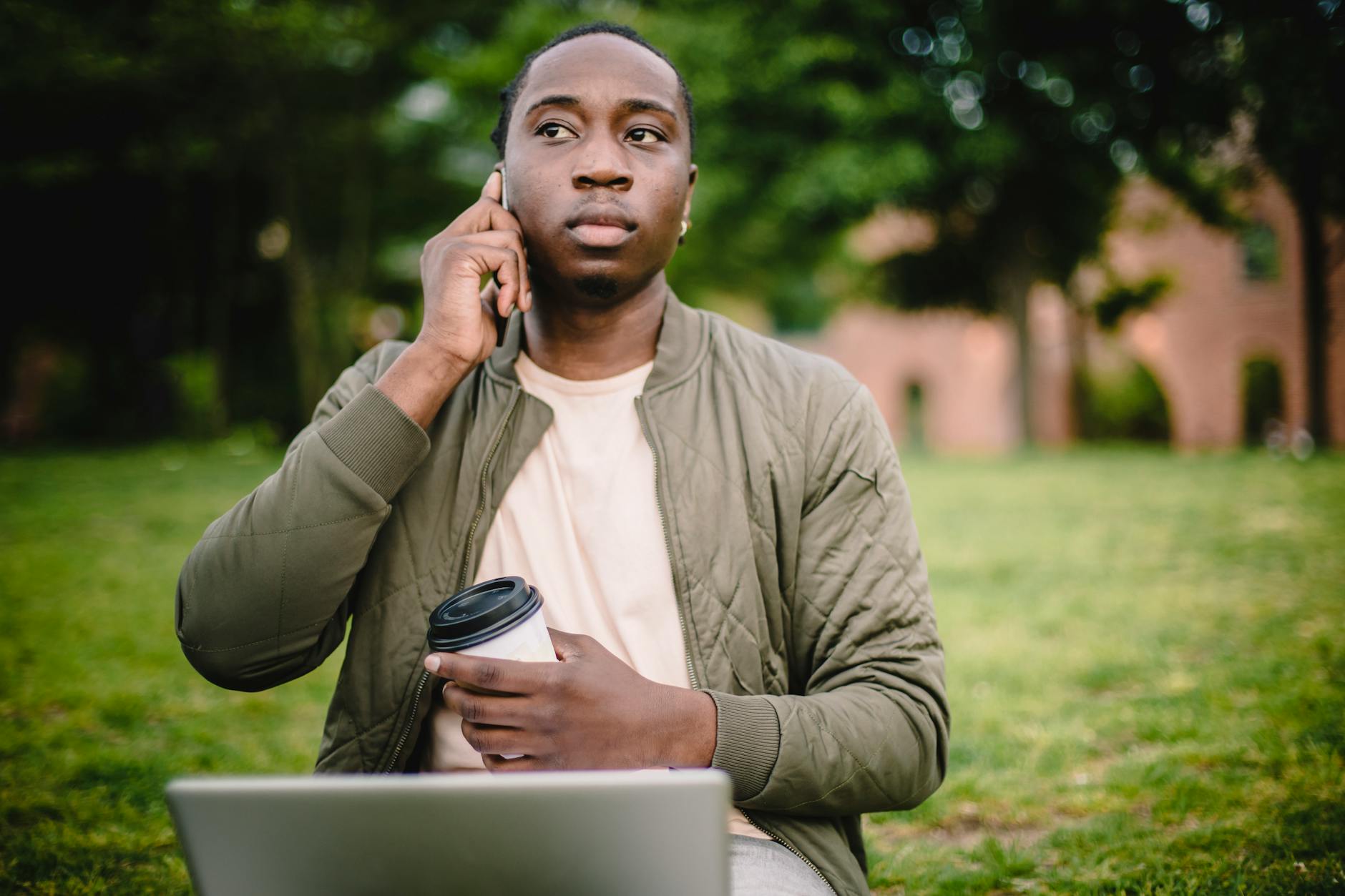 pensive young man talking on phone in green park